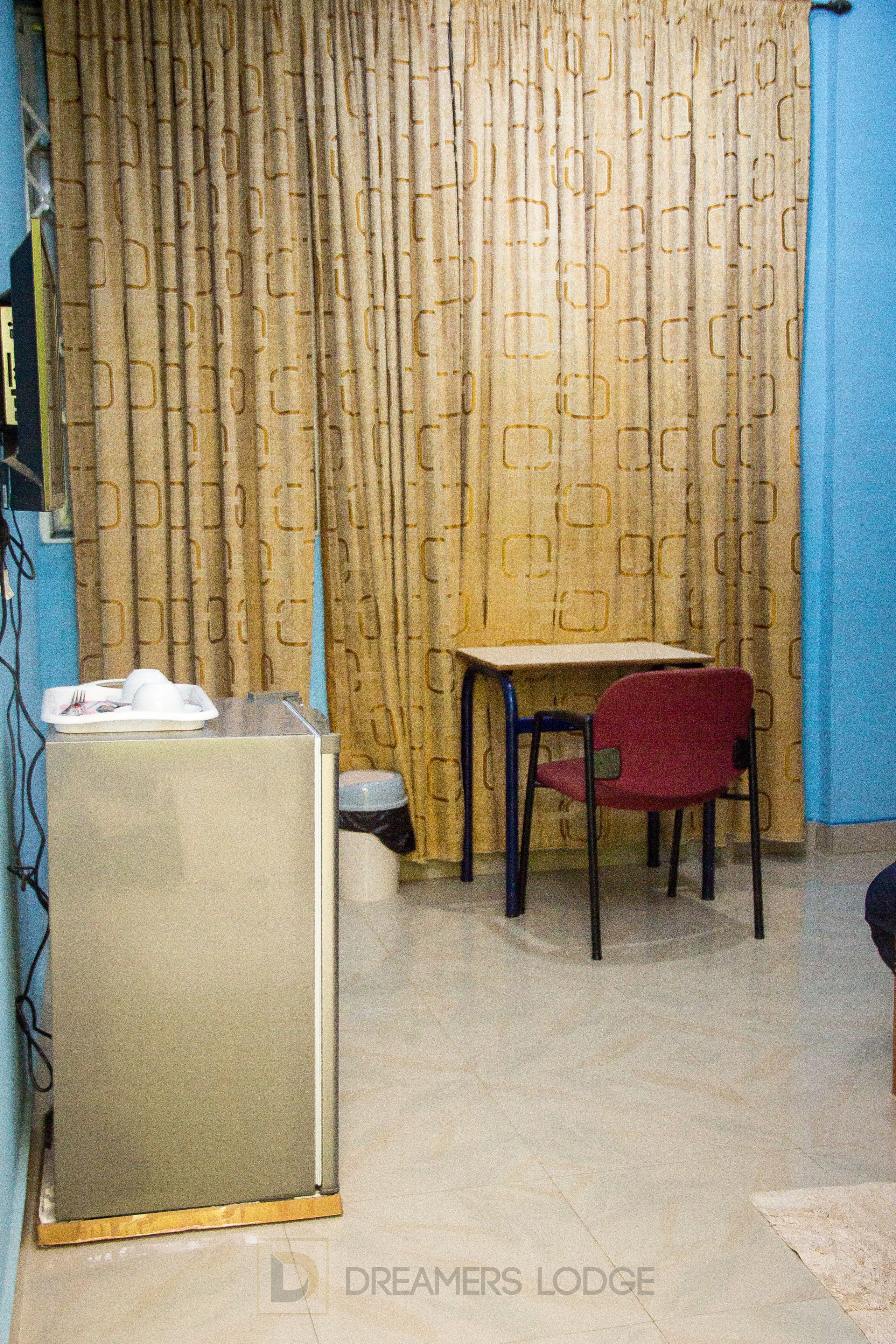 A small room with a desk, chair, and a refrigerator.
