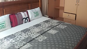 A neatly made bed with patterned bedding and pillows, a wooden headboard, a wardrobe with two doors, and an air conditioning unit on the wall. - Dreamers Lodge (Prampram)