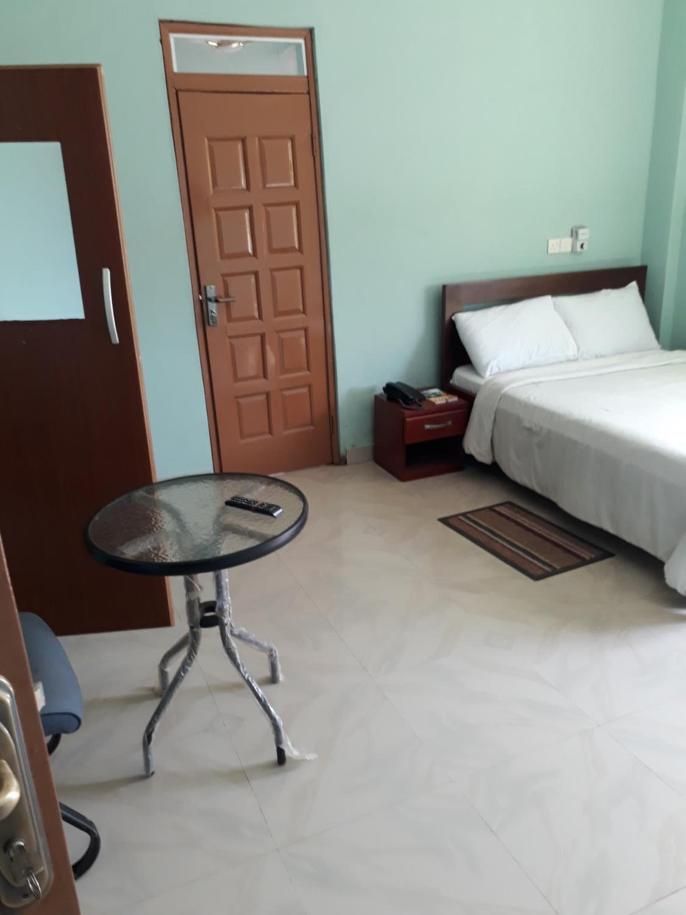 A hotel room with a bed, a small table, a door, and a nightstand.