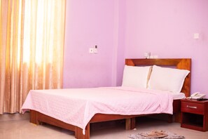 A single bed with a wooden headboard, a bedside table with a phone, and a window with curtains. - Dreamers Lodge (Prampram)