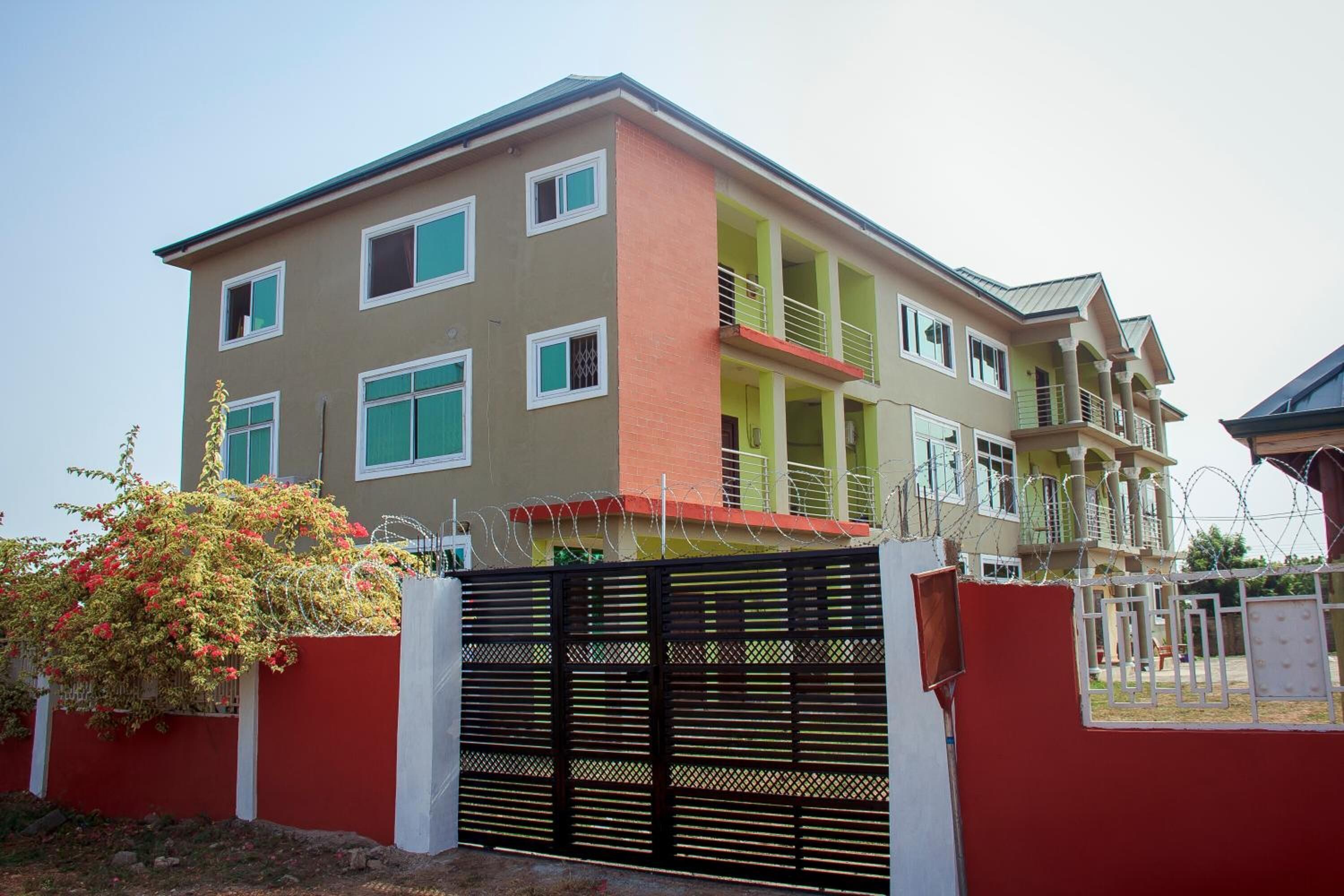 A multi-story residential building with a gated entrance, balconies, and a small garden area.