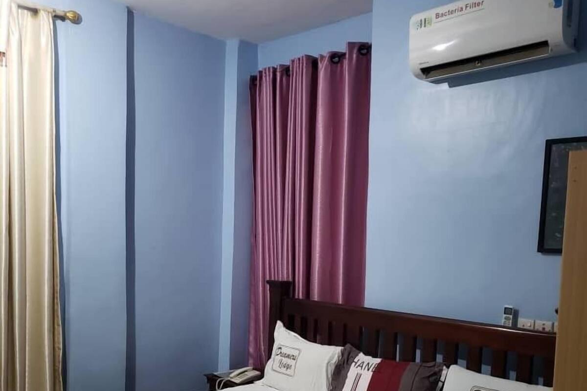 Un dormitorio con una cama, ventilador de techo, aire acondicionado y una ventana con cortinas.