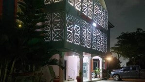 A two-story building with intricate lattice work on the facade, a covered entrance, and a paved driveway. - Dreamers Lodge (Prampram)