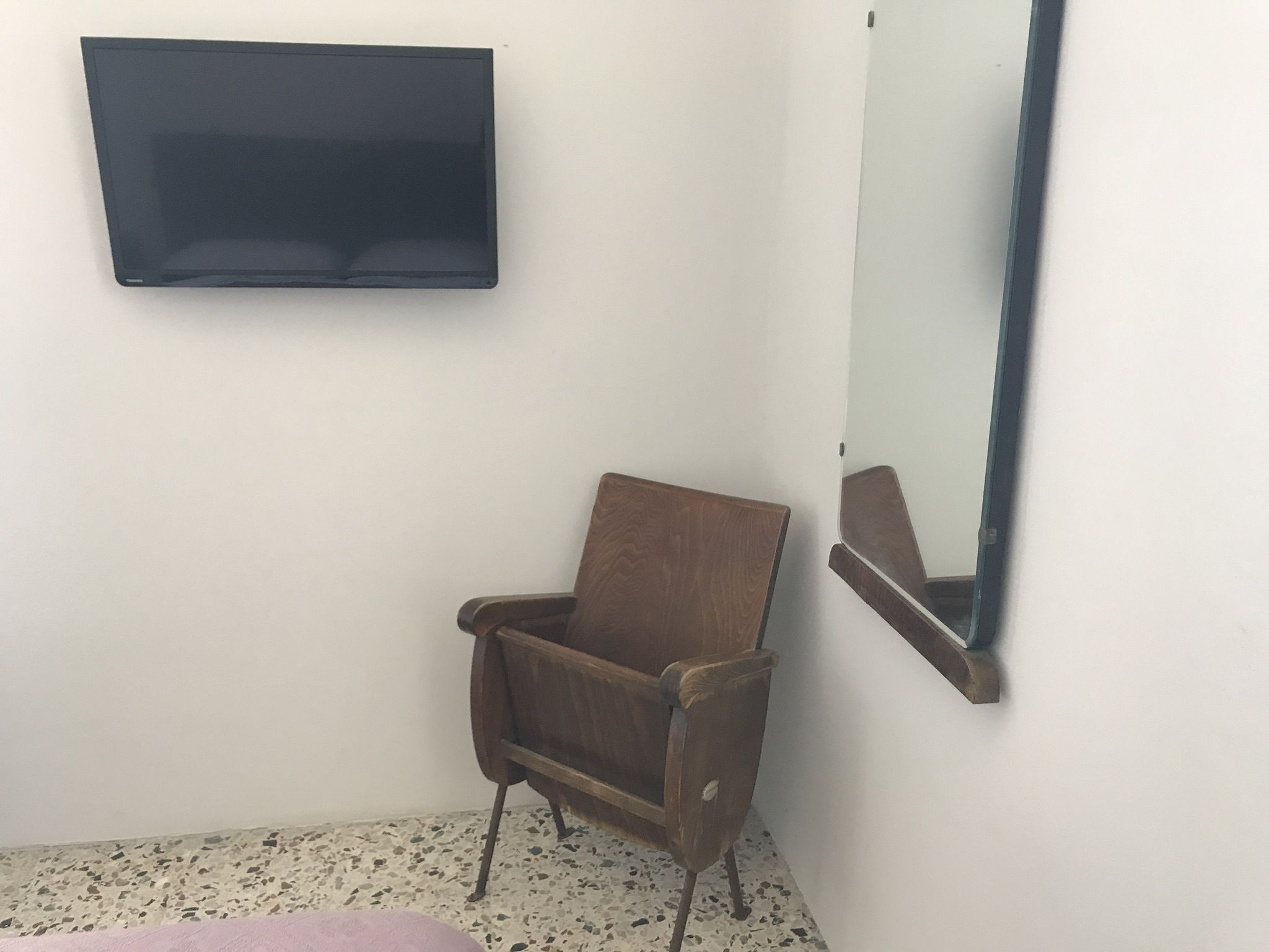 Una stanza piccola con una sedia in legno, una TV a schermo piatto e uno specchio al muro.