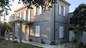 Une maison à deux étages avec un balcon, un garage et un petit jardin agrémenté de plantes en pot.