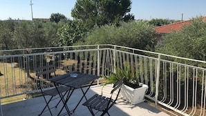 Un balcon avec une table et deux chaises, entouré d’une rambarde en métal blanc.