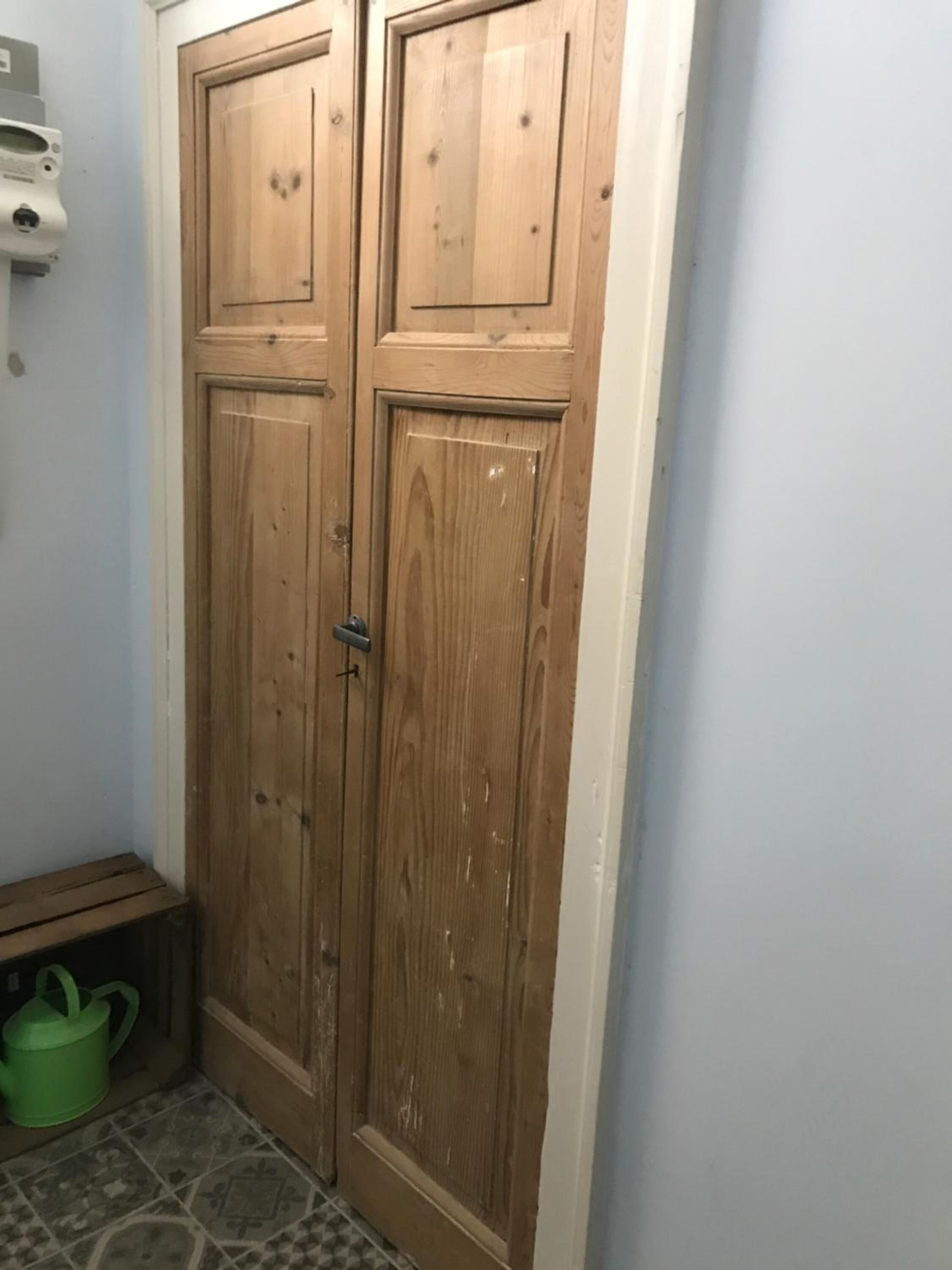 A wooden door with a handle and a green bucket on the floor.