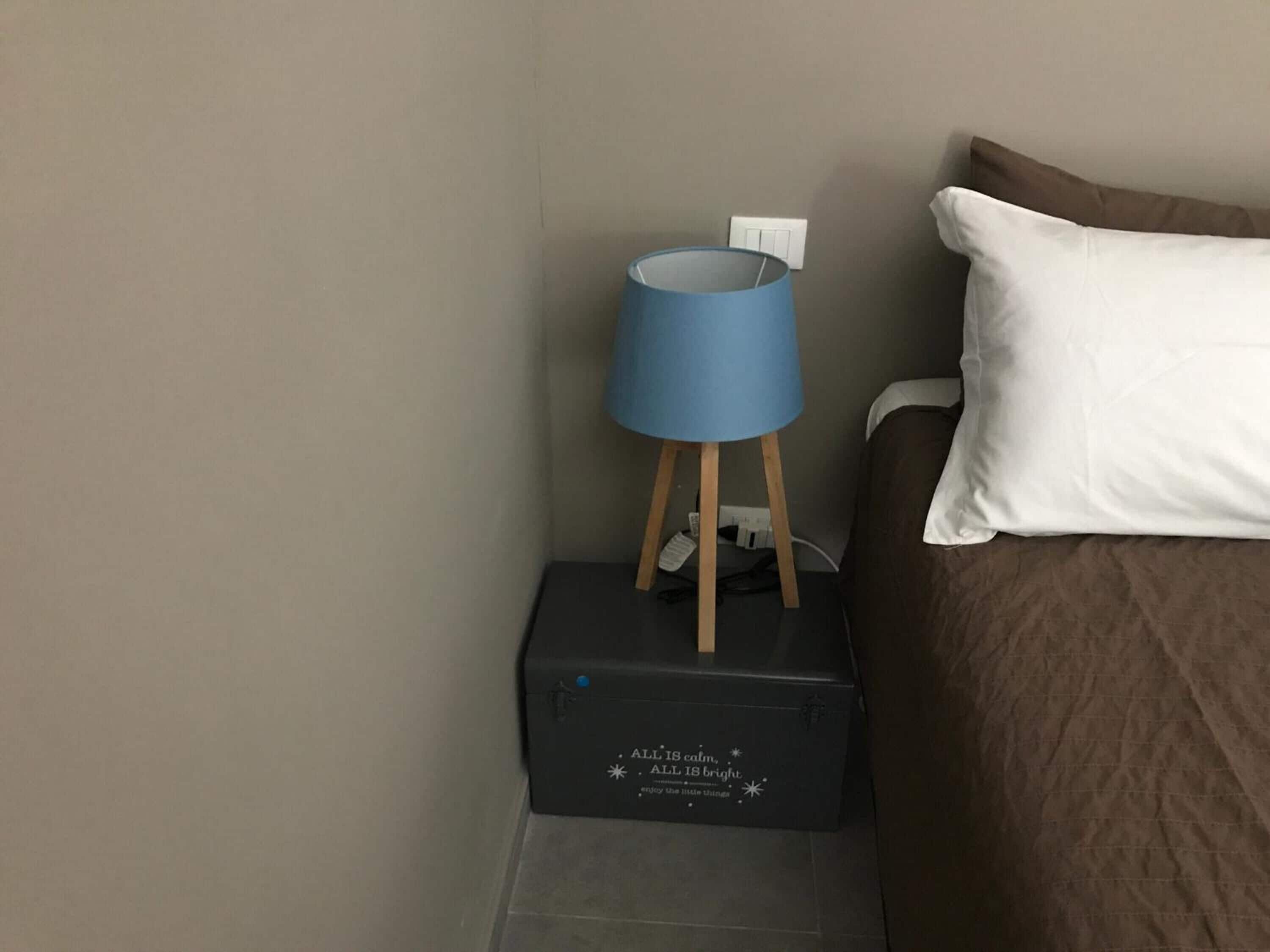 A bed with a white pillow and a blue lamp on a wooden stand, next to a black box with text.