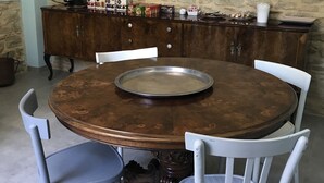Une table de salle à manger ronde en bois, surmontée d’un plateau en métal, entourée de chaises blanches, le tout placé devant un mur en pierre.