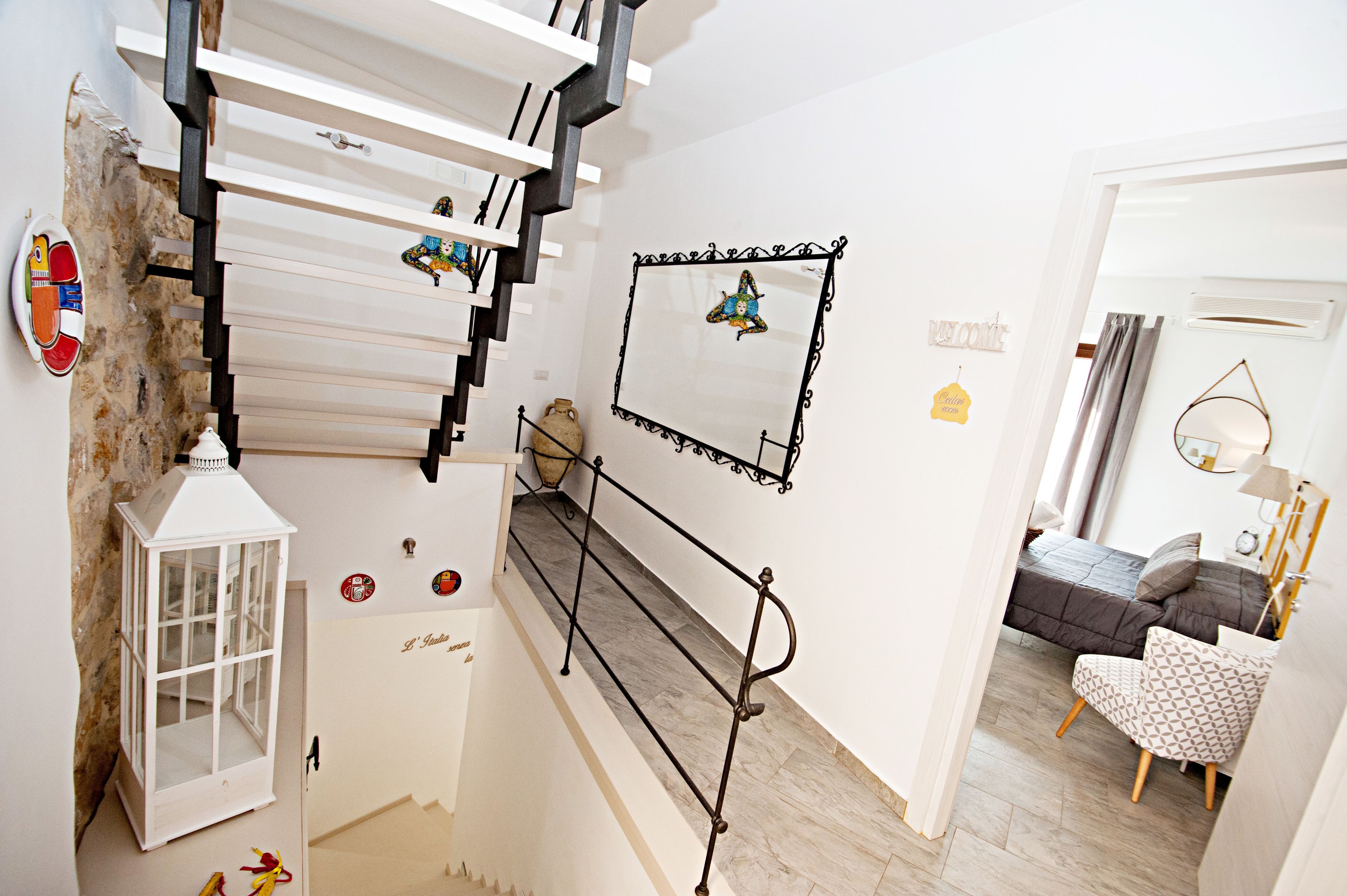 Una escalera con barandilla blanca, una mesita con un florero y una cama en la habitación contigua.