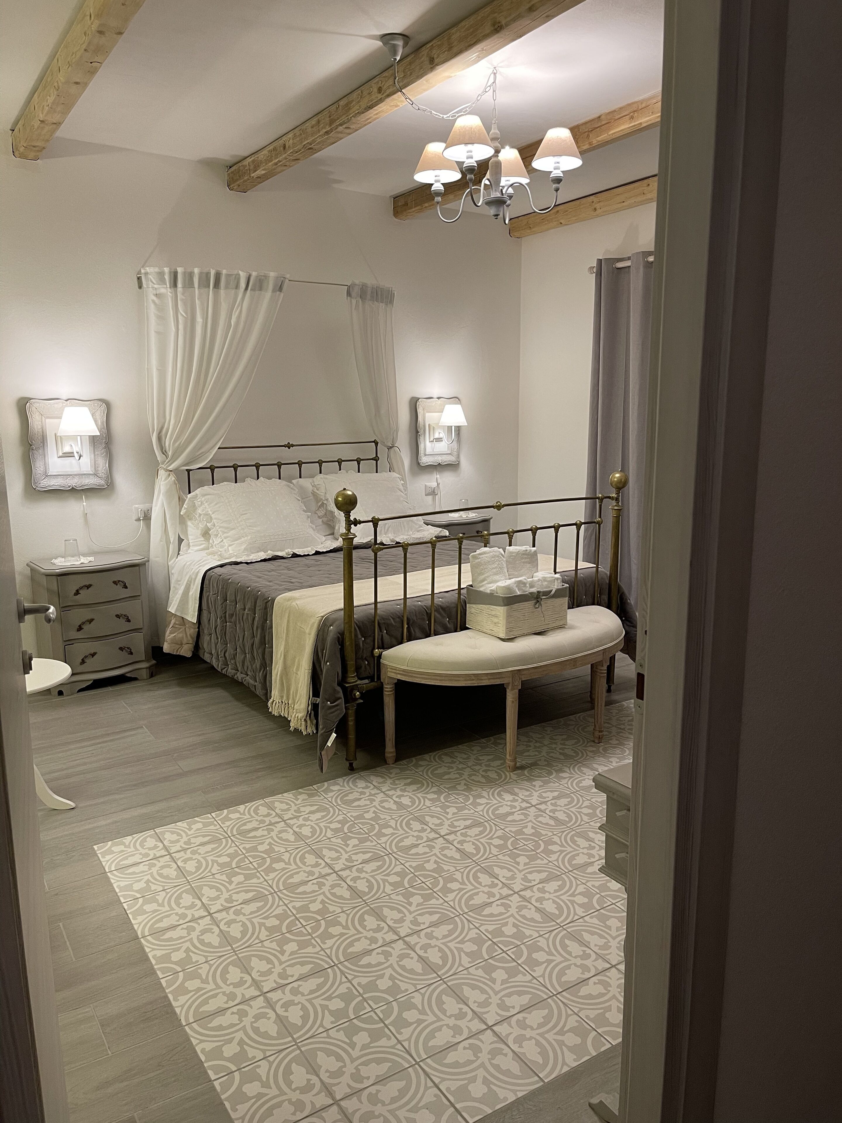 Un dormitorio con cama con dosel, una mesita de noche, un banco y una alfombra estampada.