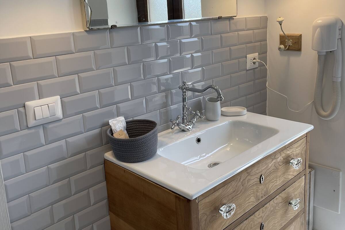 Un baño con lavamanos blanco, tocador de madera y espejo con luces empotradas.