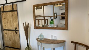 Ein Zimmer mit Holztür, einem Spiegel, einem kleinen Tisch mit einer Vase und einem Stuhl.
