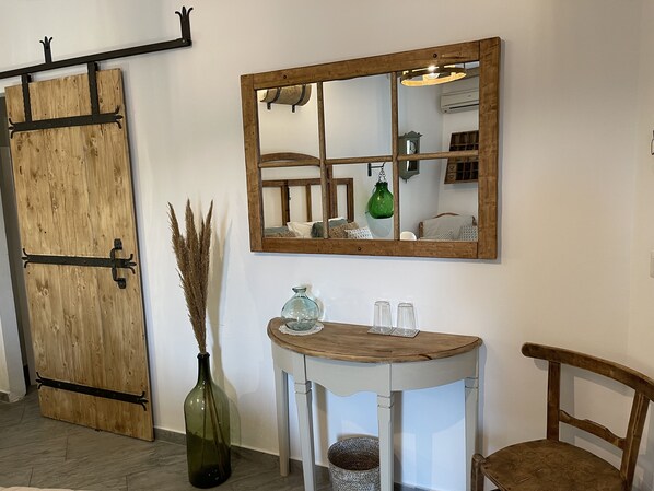 Una habitación con puerta de madera, un espejo, una mesa pequeña con un florero y una silla.