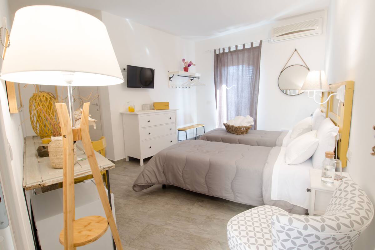 Un dormitorio con cama, escritorio, silla, televisor, espejo y ventana con cortinas.