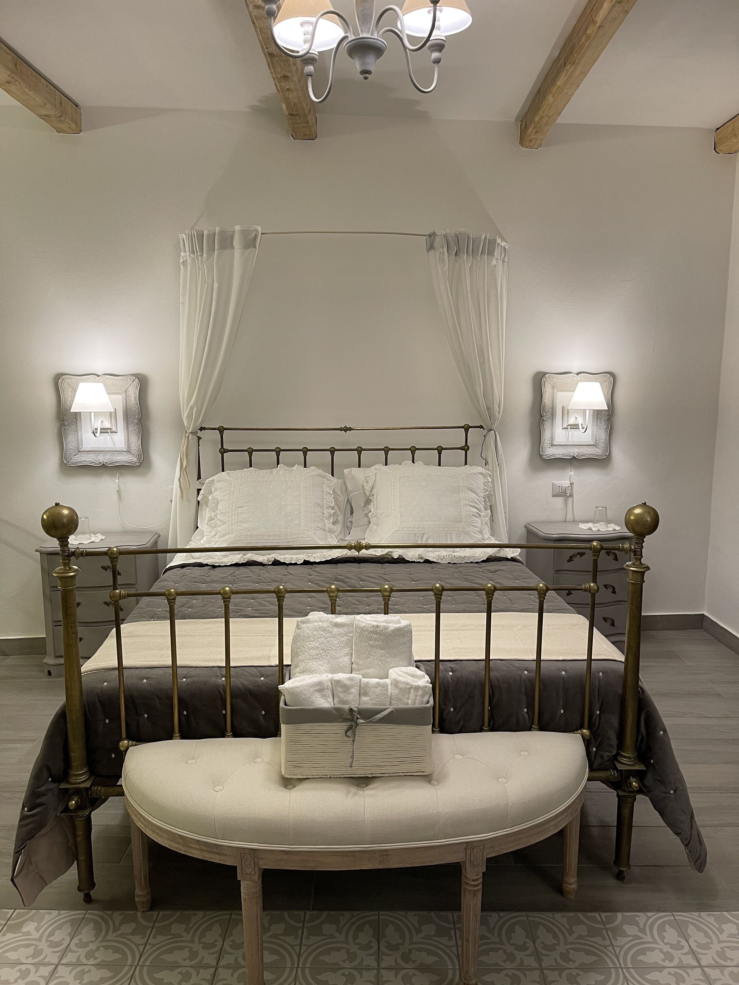 A bed with a canopy, bedside lamps, a bench, and a bedside table.