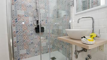 A bathroom with a glass shower enclosure, a white sink with a wooden countertop, and a mirror above the sink.