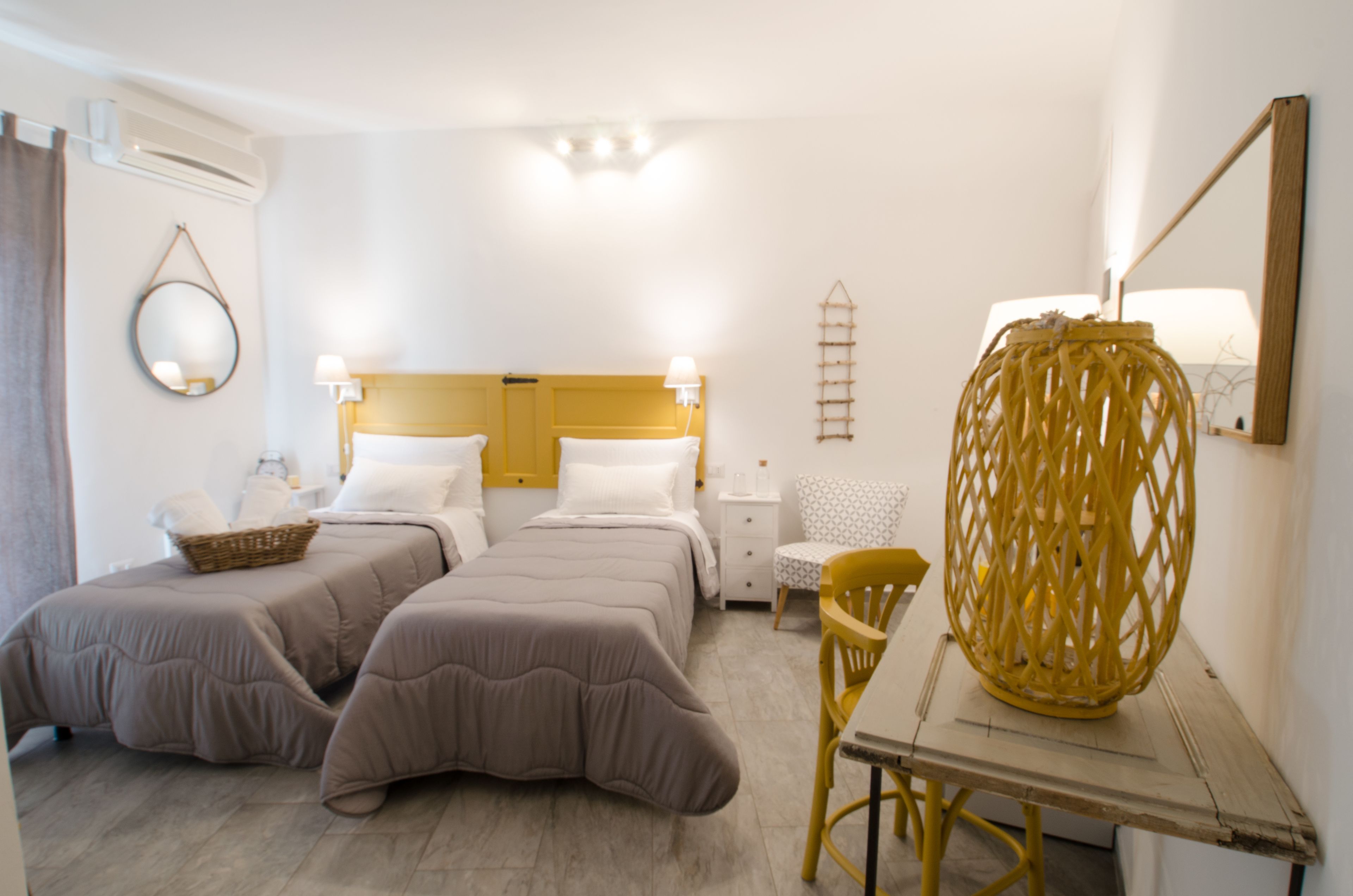 A hotel room with two beds, a wooden table, a chair, a lamp, a mirror, and a wall-mounted shelf.