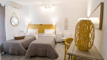 A hotel room with two beds, a wooden table, a chair, a lamp, a mirror, and a wall-mounted shelf.