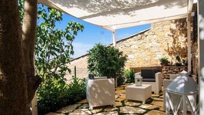 Eine Terrasse mit Steinplattenboden, Korbmöbeln und einer Steinwand im Hintergrund.