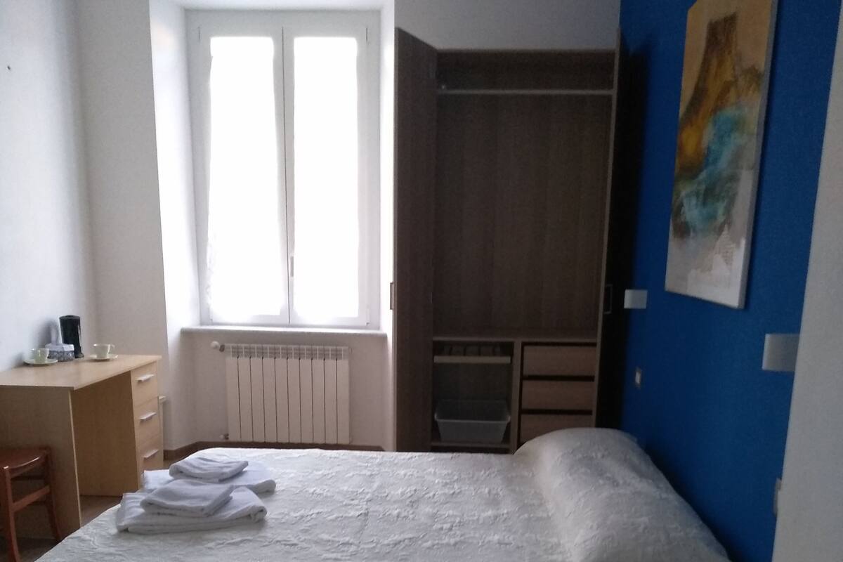A bedroom with a large bed, a desk, a chair, a wardrobe, and a radiator.
