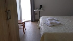 A bedroom with a bed, a small table with a cup and saucer, a chair, and a window with curtains. - Affittacamere Da Euro (La Spezia)