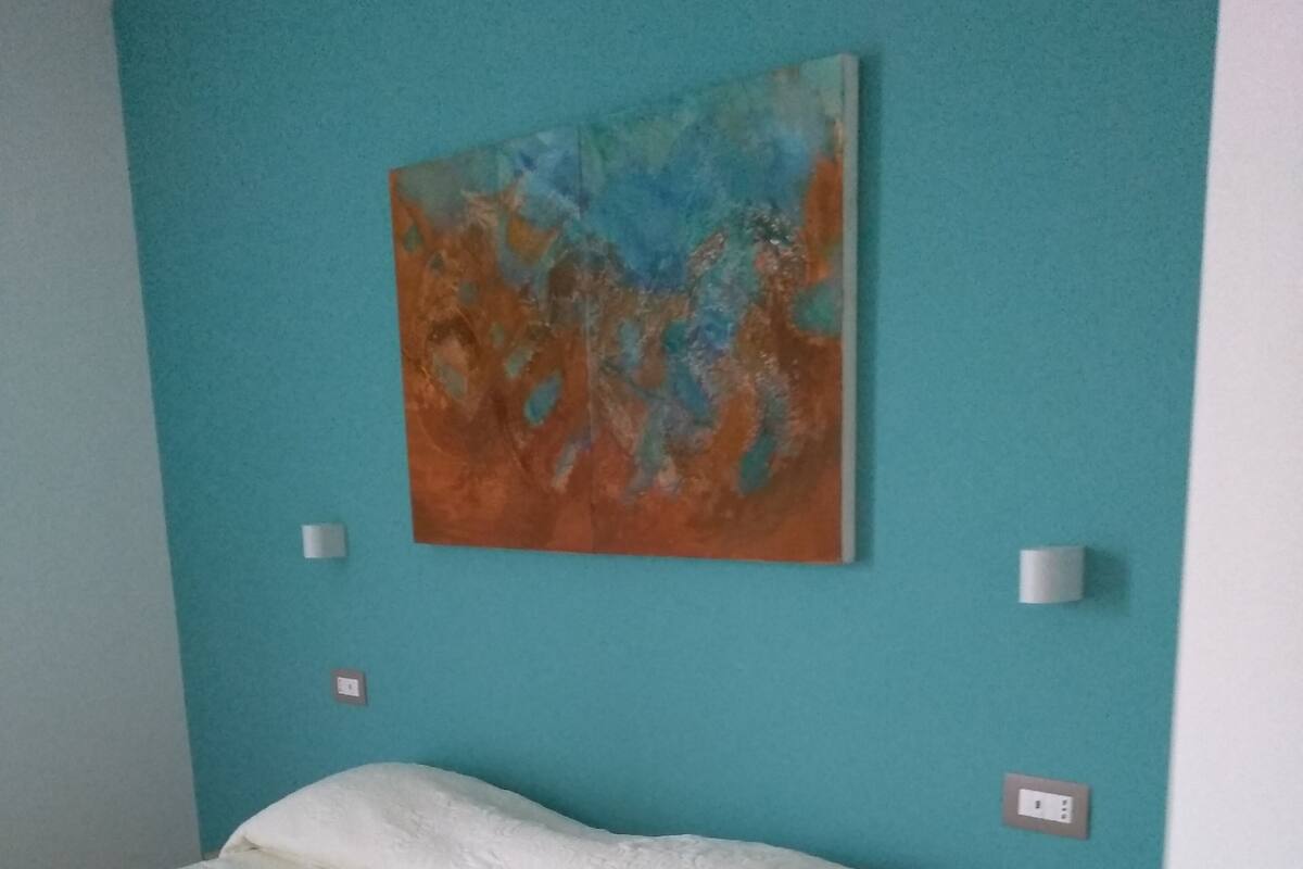 A bedroom with a bed, a nightstand, a wall-mounted painting, and a light switch.