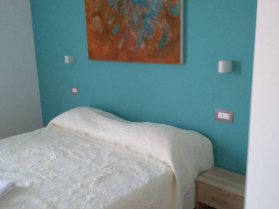 A bedroom with a bed, a nightstand, a wall-mounted painting, and a light switch.