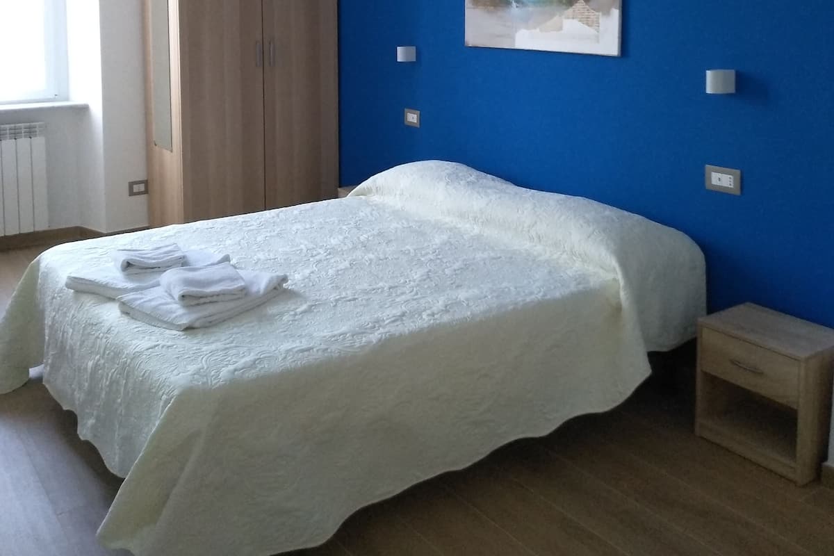 A bedroom with a bed, a wardrobe, a nightstand, a painting, and a window.