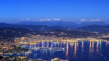 A coastal cityscape at dusk with a marina, mountains in the background, and a densely populated urban area.