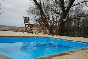 Une piscine avec des chaises longues en bois et un grand arbre en arrière-plan.