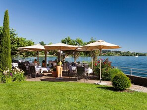 An outdoor dining area with tables and chairs, umbrellas, and a view of a lake.