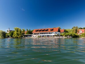 A waterfront hotel with a red roof, multiple windows, and a view of the water.