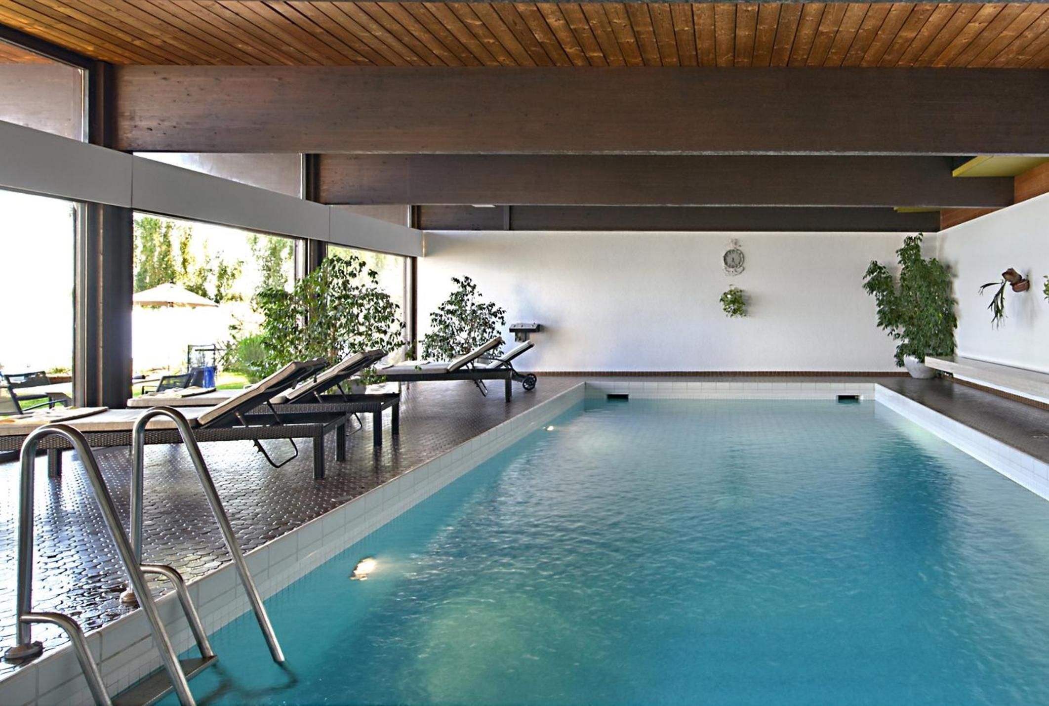 Une piscine intérieure offrant une vue dégagée sur l’eau, avec un plafond en bois et quelques chaises longues.