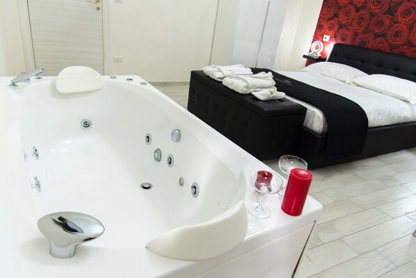 Een moderne hotelkamer met een groot, wit bad, een zwart nachtkastje met handdoeken en een rode accentmuur.