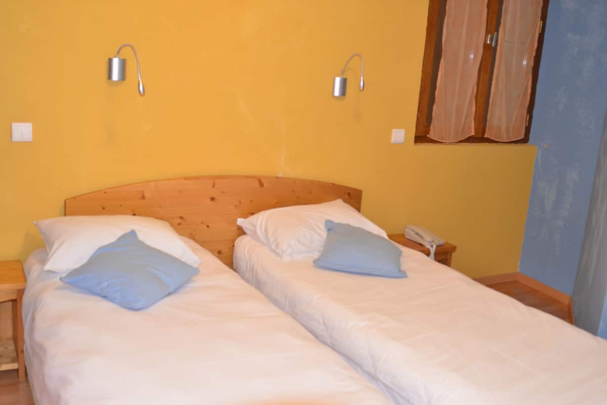 A room with two single beds, wooden headboards, white bedding, and bedside lamps.