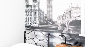 A bedroom with a bed, a wooden dresser, and a wall mural of London landmarks. - Leo Hostel (Poznań)