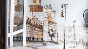 A view through a window of a building with a tiled floor, a table with a metal frame, and a reflection of a cityscape with buildings and a clock tower. - Leo Hostel (Poznań)