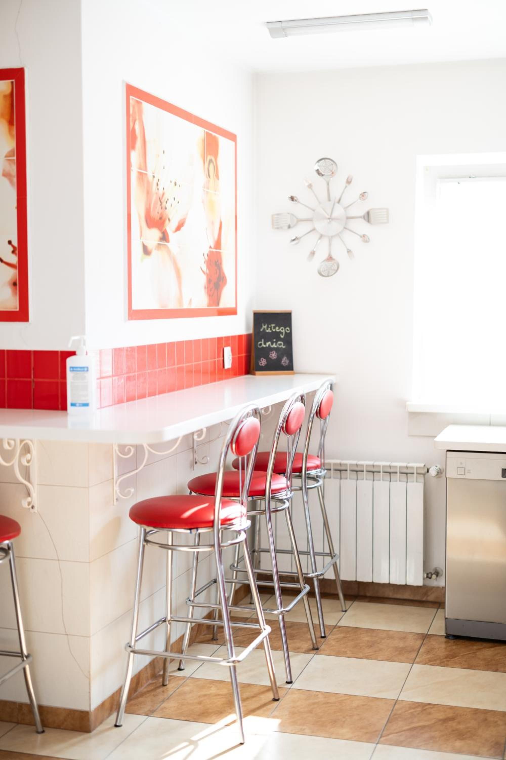 Una cocina con encimera blanca, sillas rojas, lavavajillas blanco y salpicadero con azulejos rojos.