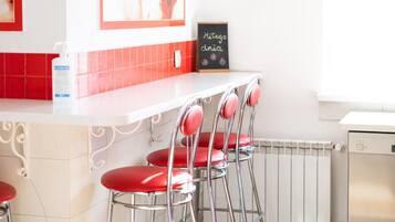 Una cocina con encimera blanca, sillas rojas, lavavajillas blanco y salpicadero con azulejos rojos.