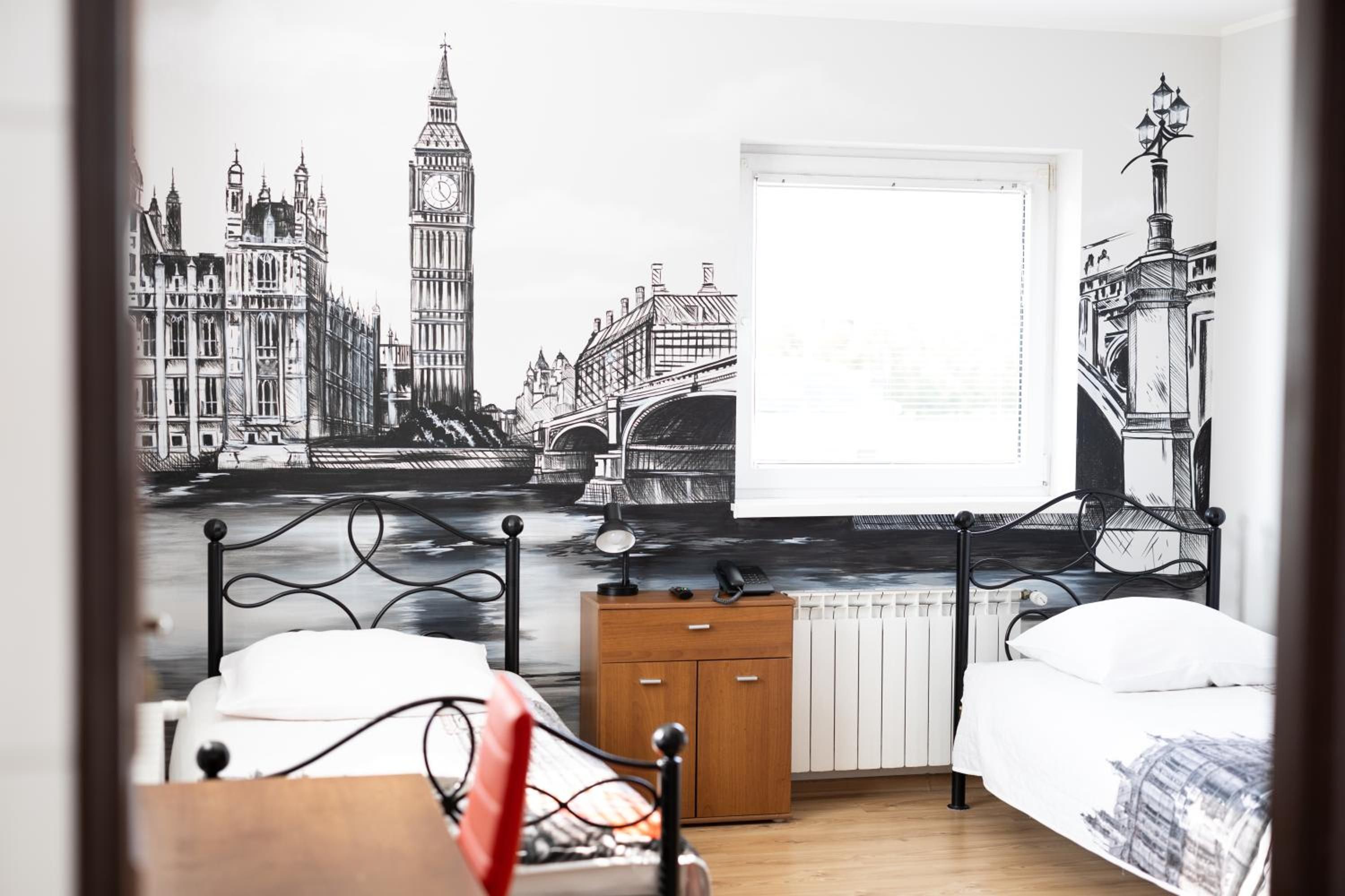 Un dormitorio con un mural de puntos emblemáticos de Londres, una cama, una mesita de noche y un radiador.
