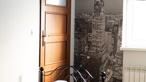 A bedroom with a bed, a wooden door, a radiator, and a cityscape poster on the wall. - Leo Hostel (Poznań)