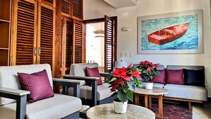 A well-lit living area with wooden louvered doors, a sofa set, a coffee table, and a painting of a boat on the wall. - Casa Carmen - Boutique B&B (Puerto Vallarta)