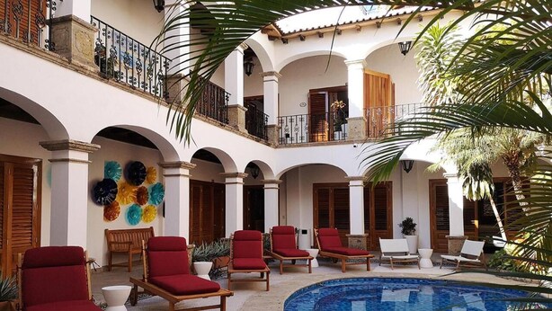 A poolside area with red lounge chairs, a tiled pool, and a balcony with a railing. - Casa Carmen - Boutique B&B (Puerto Vallarta)