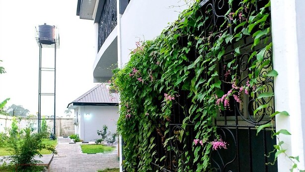 A building with a white exterior, a metal water tank, and a pathway leading to a gated entrance. - The Good House PHC (Port Harcourt)