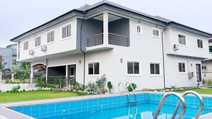 A modern two-story house with a balcony, a swimming pool, and a covered outdoor area. - The Good House PHC (Port Harcourt)