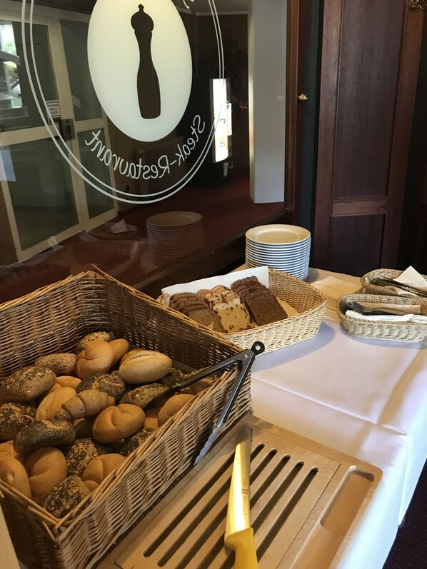 Una mesa de buffet con diferentes panes y pasteles, un cuchillo y platos apilados.