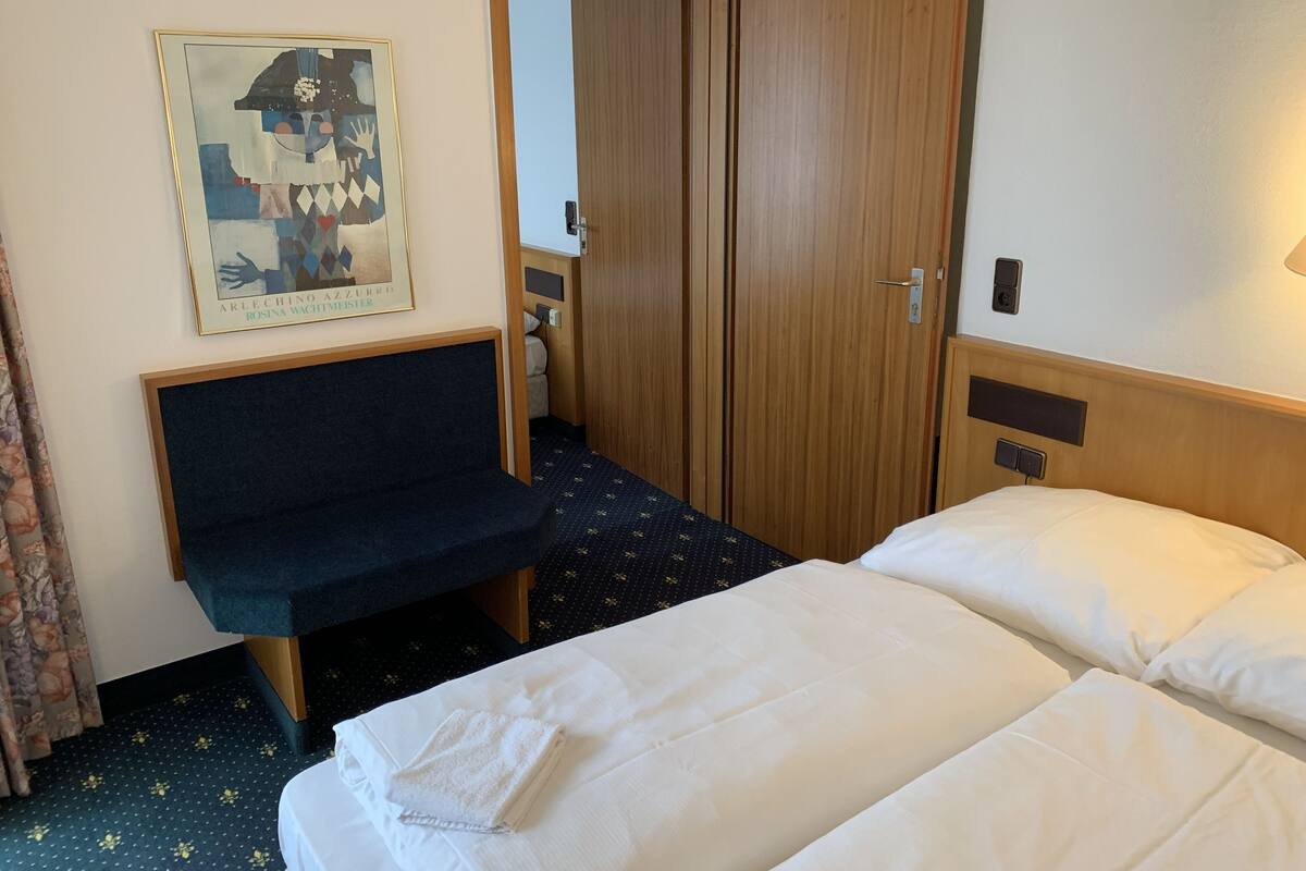 A hotel room with a bed, a sofa, a wardrobe, and a poster on the wall.