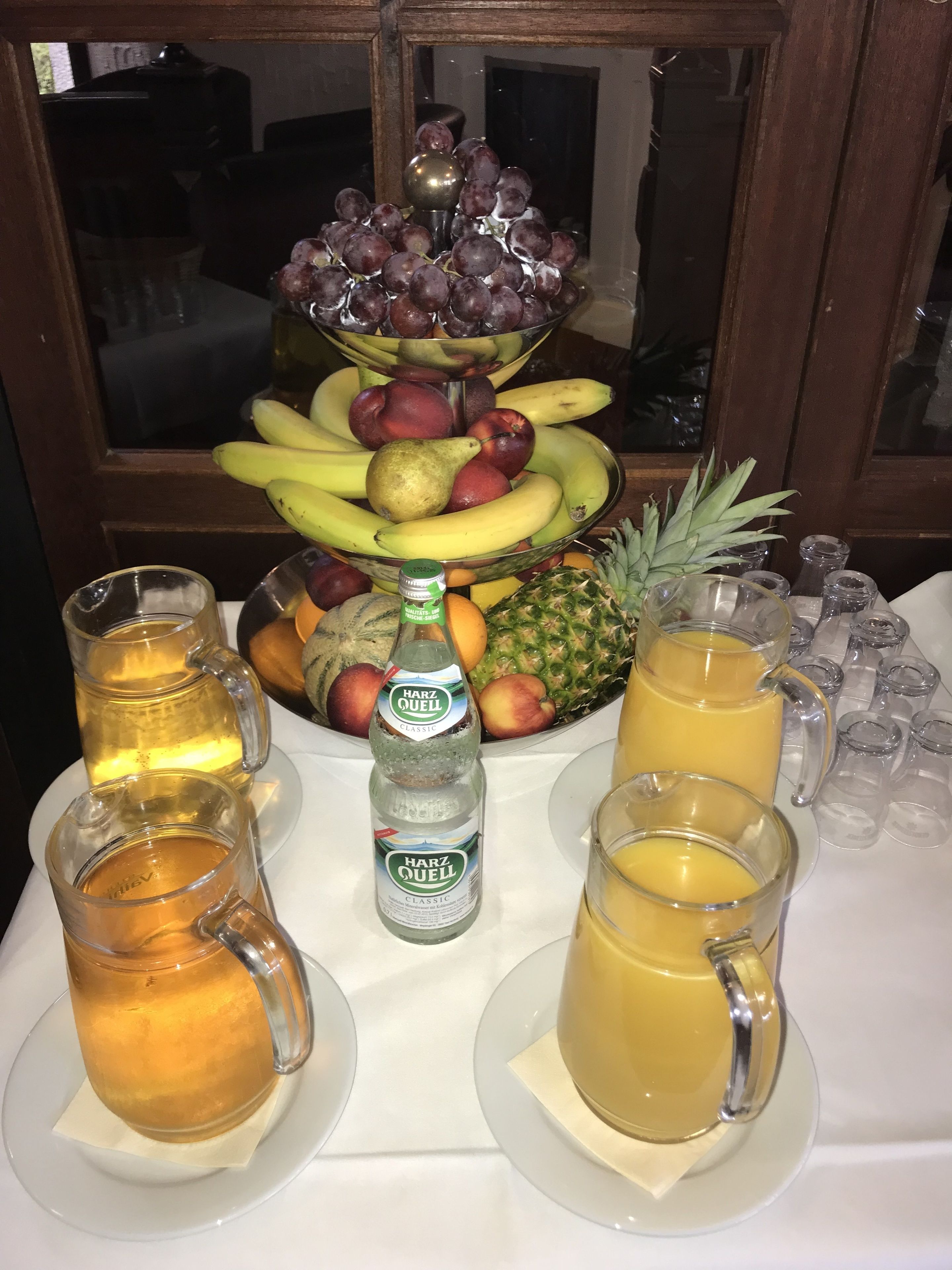 A fruit arrangement on a table with two pitchers of beverages and a bottle of Harz Quell Classic.
