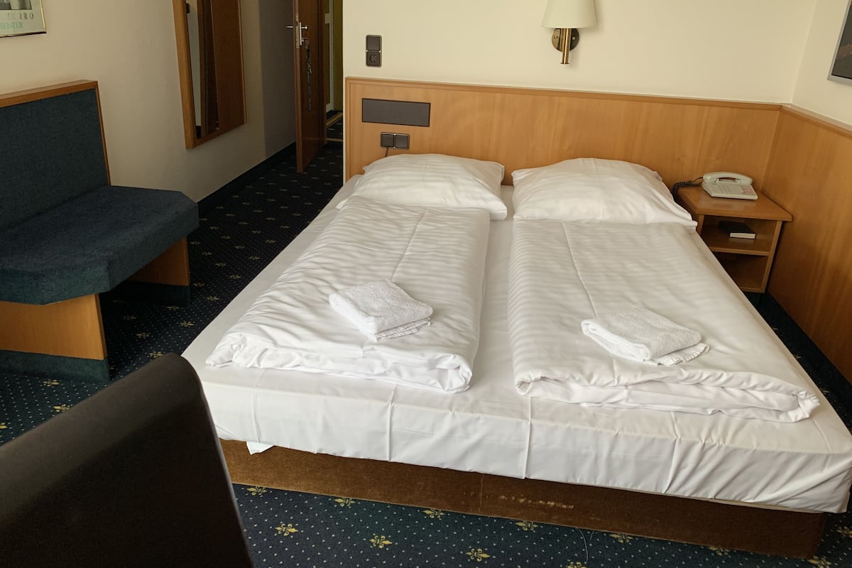 A hotel room with two beds, a desk, a chair, a lamp, and a phone on the nightstand.